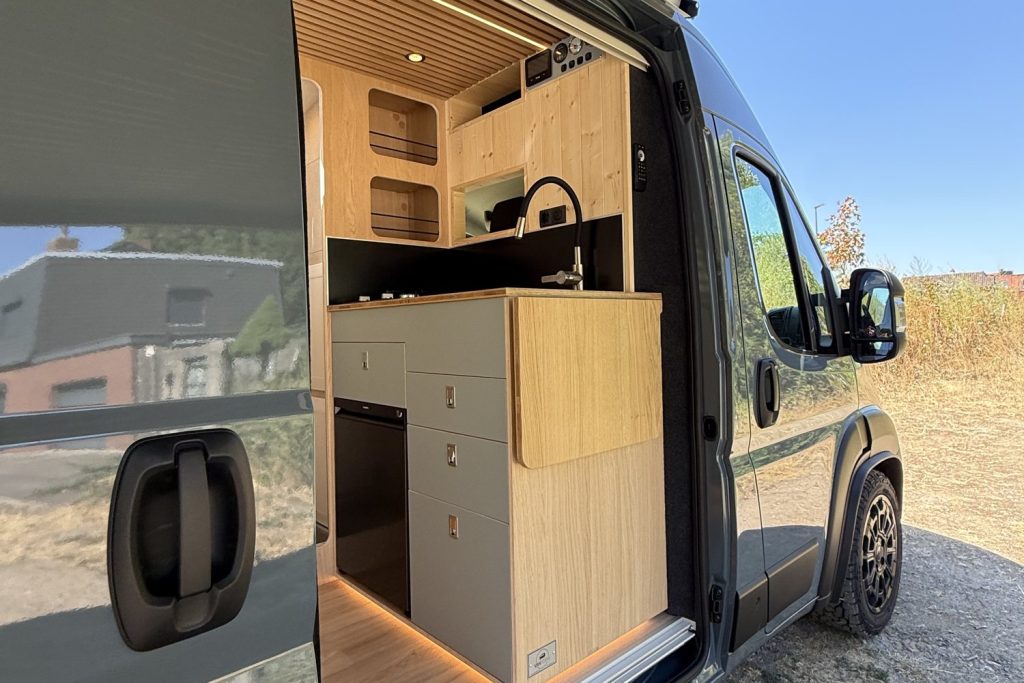 Cuisine en bois d’un van aménagé sur mesure par Vanatipik, vue par la porte latérale ouverte